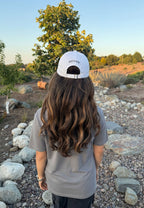 White baseball cap worn back with small logo on the crown